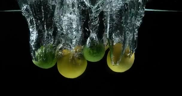 Желтый, цитрусовый лимонный, апельсиновый, плоды, падающие в воду на фоне черного, медленное движение 4K — стоковое видео