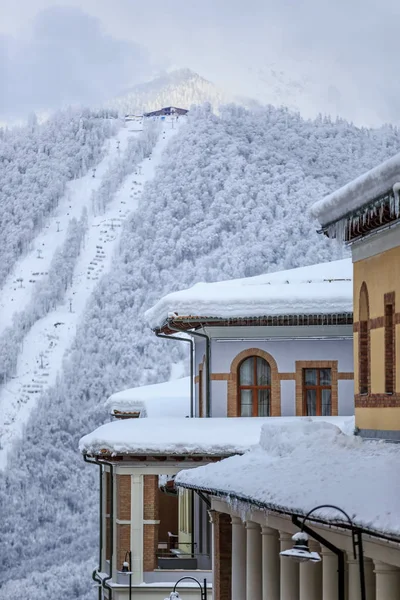 Заснеженные крыши отелей зимнего горного курорта Горький город с канатной дорогой на фоне вертикальных пейзажей — стоковое фото