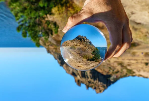 Krím, Fekete-tenger. Scenic landscape of Karadag mountain view through glass ball in hand on sunny clear blue sky day. Koktebel hegycsúcsa. Népszerű turisztikai célpont — Stock Fotó