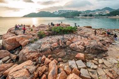 Hong Kong, Çin - 30 Ocak 2016: İnsanlar Hong Kong 'daki Stanley Körfezi kıyılarında dinleniyor. Su, dağlar, kayalar ve binalarla güzel manzaralı günbatımı manzarası