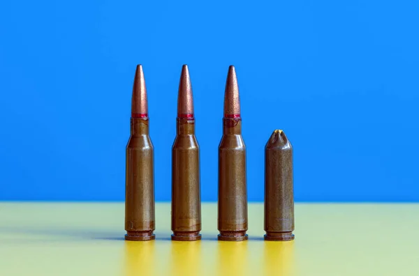 Live and blank gun cartridges on blue yellow background close up. War and peace concept, love and hope concept. Ukraine flag colors