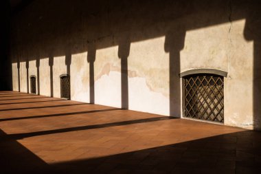 Gün batımı, sütunun gölgelerini çelik çubuklar ve kahverengi kiremitlerden oluşan bir çiçekle ele geçirilen pencerelerle galeriye atar.