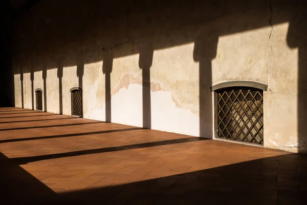 Gün batımı, sütunun gölgelerini çelik çubuklar ve kahverengi kiremitlerden oluşan bir çiçekle ele geçirilen pencerelerle galeriye atar.