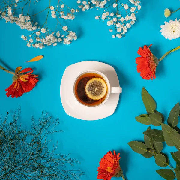 Одна Чашка Чая Лимоном Синем Фоне Красные Цветы Вокруг Листья — стоковое фото