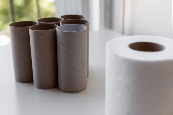 Group of empty toilet paper rolls are looking at the blurry full roll in the foreground on white table