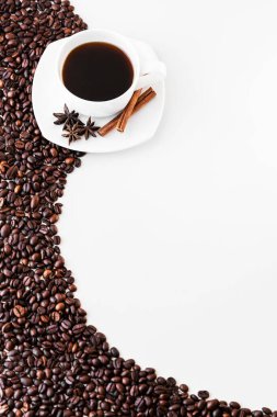 Beyaz fincanda kahve ve çay tabağı, tarçın ve yıldız anason çiçekleri, beyaz arka planda kahve çekirdekleri serpiştirilmiş. Kafe, restoran ya da kafeterya menüsü için harika bir fikir.