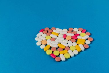 Mavi arka planda kalp şeklinde katlanmış birçok farklı hap ve tablet var. Bir sürü hap ve tablet. Mesaj için yer var. Sağlık hizmetleri. Üst Manzara. Uzayı kopyala Yeni imaj. Eczacılık. - Yakın çekim. Yumuşak odak