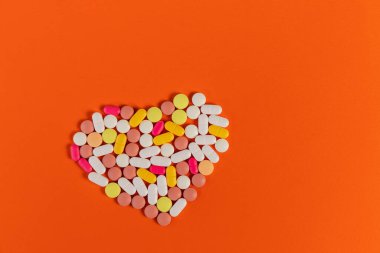 Turuncu arka planda kalp şeklinde katlanmış birçok farklı hap ve tablet var. Mesaj için yeri olan bir sürü hap ve tablet. Sağlık hizmetleri. Üst Manzara. Uzayı kopyala Yeni imaj. Eczacılık hapları. Düz Yatay