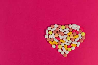 Pembe arka planda kalp şeklinde katlanmış birçok farklı hap ve tablet var. Mesaj için yeri olan bir sürü hap ve tablet. Sağlık hizmetleri. Üst Manzara. Uzayı kopyala Yeni imaj. Farmasötik resim