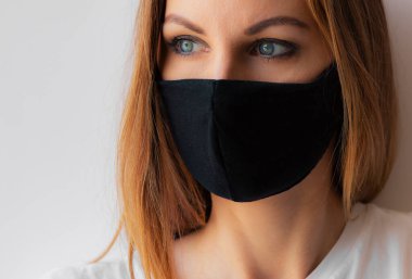 Siyah tıbbi maskeli ve beyaz arka planda beyaz tişörtlü genç bir kadının yakın plan portresi. Karantina, koronavirüs salgını, covid-19. Evde kal konsepti. Virüs koruması.