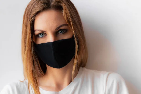Siyah tıbbi maskeli ve beyaz arka planda beyaz tişörtlü genç bir kadının güzel yakın plan portresi. Karantina, koronavirüs salgını, covid-19. Evde kal konsepti. Virüs koruması.