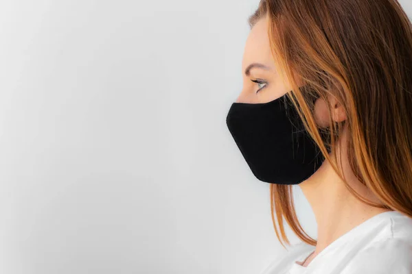 Siyah tıbbi maskeli ve beyaz tişörtlü bir kadının profili. Koronavirüs salgını karantinası az önce sona erdi, covid-19. Evde kal konsepti. Virüs koruması. Yeni gerçeklik