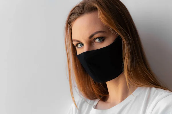 Siyah tıbbi maskeli ve beyaz arka planda beyaz tişörtlü genç bir kadının yakın plan portresi. Karantina, koronavirüs salgını, covid-19. Evde kal konsepti. Virüs koruması.