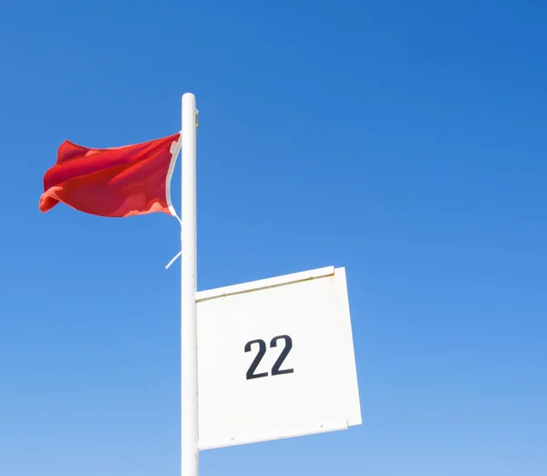 Bandeira vermelha em uma praia acenando acima do céu azul — Fotografia de Stock