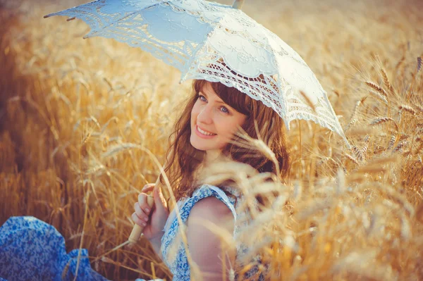 Fille souriante assise dans un champ de blé sous un parasol blanc — Photo