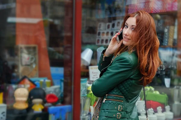 Рыжая женщина с телефоном в витрине магазина — стоковое фото
