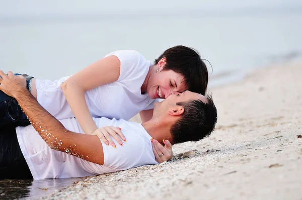Happy in the arms of a young couple lying on the sand beach — Stock Photo, Image