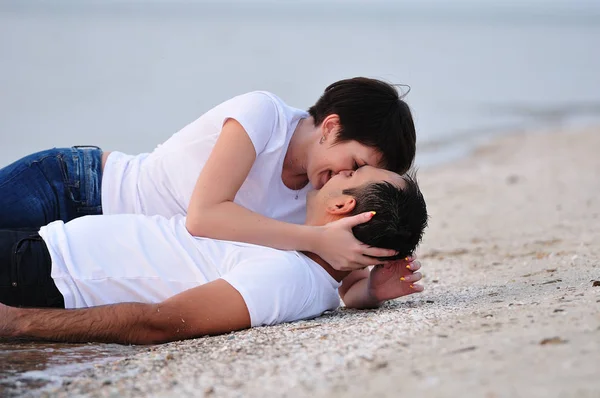 Szczęśliwa w ramionach młodej pary, leżąc na plaży piasek — Zdjęcie stockowe
