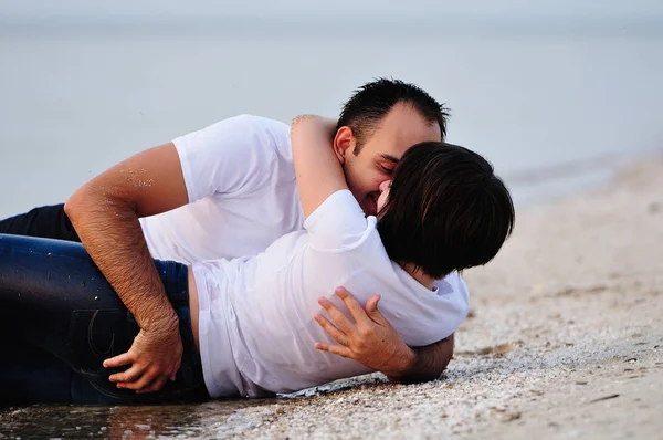 Feliz en los brazos de una joven pareja acostada en la playa de arena —  Fotos de Stock