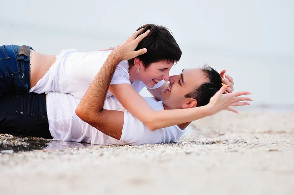 Feliz en los brazos de una joven pareja acostada en la playa de arena —  Fotos de Stock