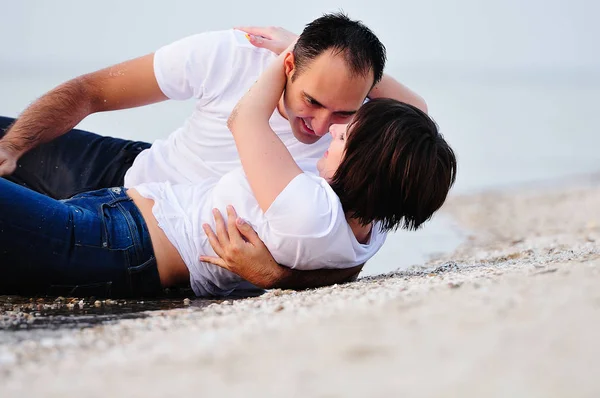 Feliz en los brazos de una joven pareja acostada en la playa de arena —  Fotos de Stock