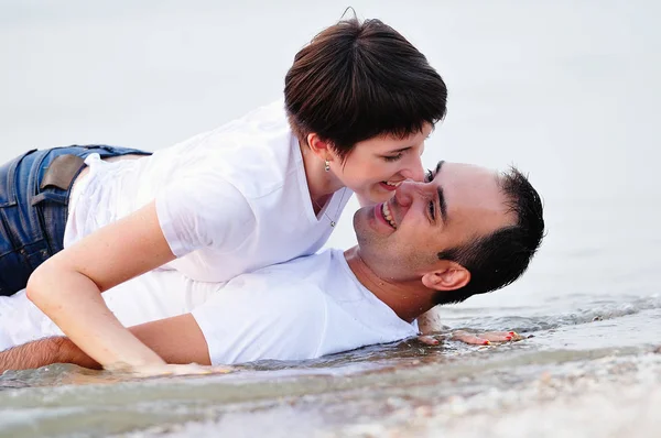 Feliz nos braços de um jovem casal deitado na praia de areia — Fotografia de Stock