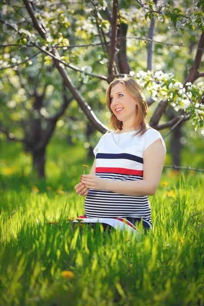 Zwangere jonge vrouw in de bloeiende lentetuin — Stockfoto