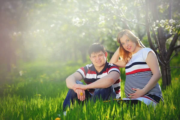 Mladí těhotná pár sedí na zelené trávě na jaře — Stock fotografie