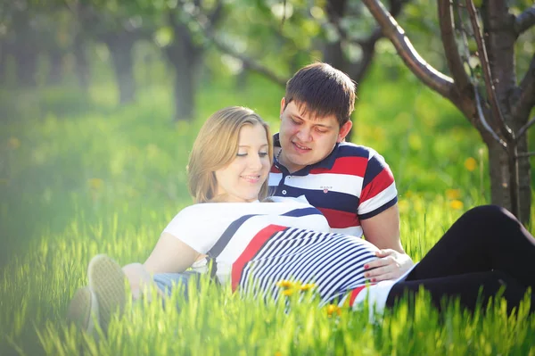 Jovem casal grávida sentado na grama verde na primavera — Fotografia de Stock