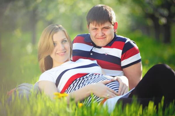 Jong zwanger koppel zittend op het gras in de lente — Stockfoto