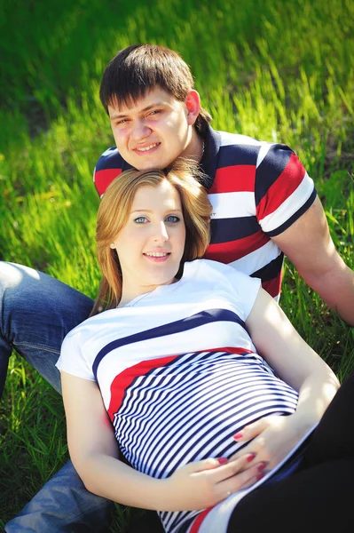 Ilkbaharda yeşil çimenlerin üzerinde oturan genç hamile Çift — Stok fotoğraf