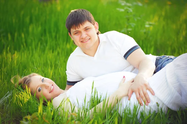 Jovem casal grávida sentado na grama verde na primavera — Fotografia de Stock