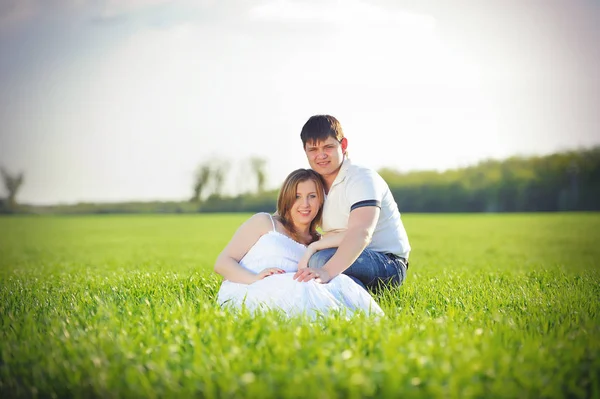 Jong zwanger koppel zittend op het gras in de lente — Stockfoto