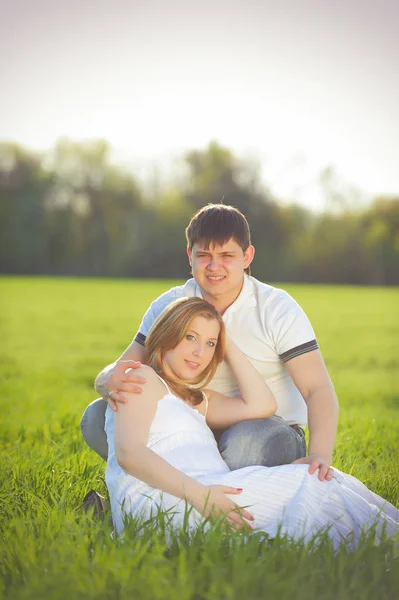 Молода вагітна пара сидить на зеленій траві навесні — стокове фото
