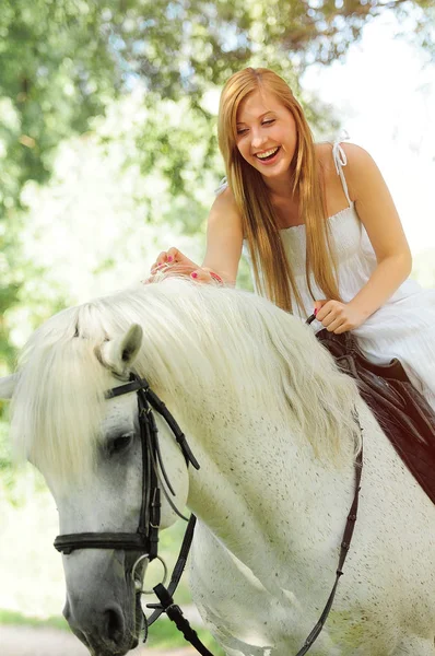 Jovem mulher em um vestido branco em um cavalo branco — Fotografia de Stock