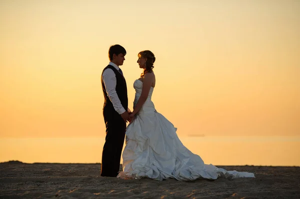Bruid en bruidegom lopen op het zand aan de oever — Stockfoto