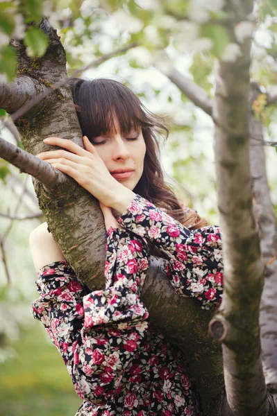 Mooie vrouw in jurk knuffelen boom in de tuin — Stockfoto