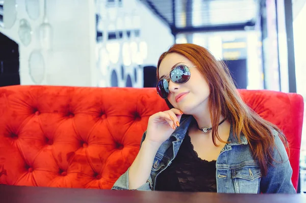 Женщина в очках на красном диване в уличном кафе — стоковое фото