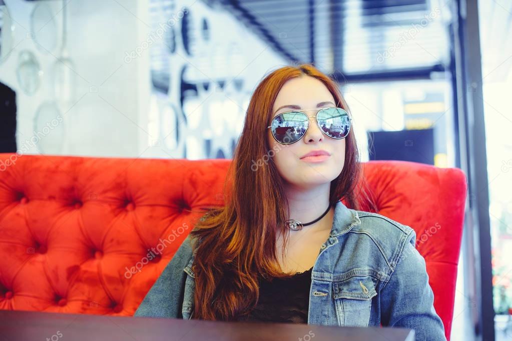 oung woman with glasses on a red sofa in a street cafe