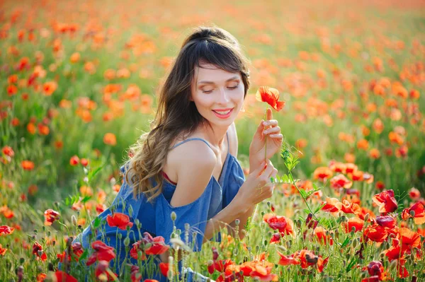 Mulher de beleza em um vestido azul sorri em um campo de papoula ao pôr do sol, limpeza e inocência, unidade com a natureza — Fotografia de Stock