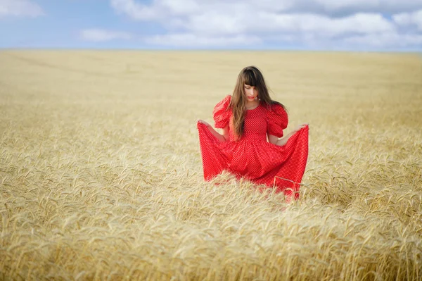 Mujer en un campo de trigo en un vestido largo rojo, sostiene en las manos . — Foto de Stock