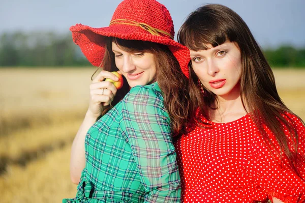 Two cheerful women in a wheat field at sunset in a blue and red long air dress. — Stock Photo, Image