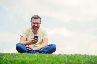 Doğa ve teknoloji. Bir sakallı bir adam yatıyor bir yeşil çim onun elinde bir akıllı telefon ile güç banka şarj.