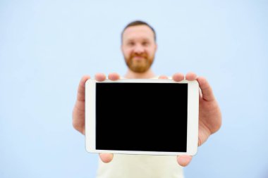 Üzerinde mavi bir arka plan, yakın çekim, metniniz için mutlu yakışıklı genç adam bir şey bir tablet üzerinde gösterilen sakallı izole