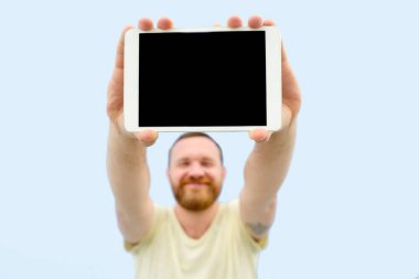 Üzerinde mavi bir arka plan, yakın çekim, metniniz için mutlu yakışıklı genç adam bir şey bir tablet üzerinde gösterilen sakallı izole