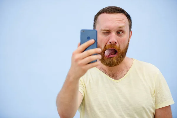 Člověk dělá obličeje v legrační a vtipné telefon ukazuje jazyk, reklamní společnost — Stock fotografie