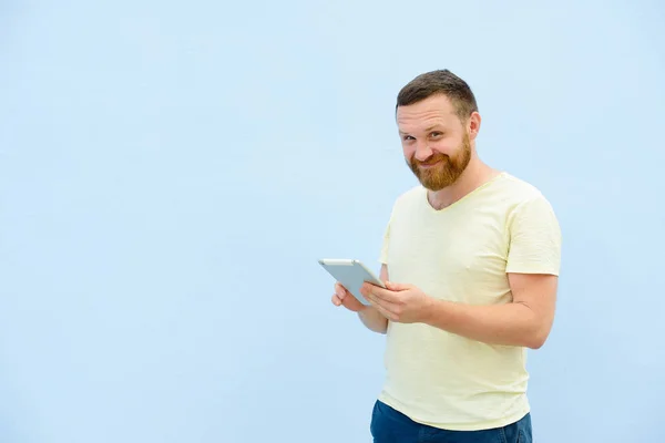 Pohledný mladý muž s bradkou, hledá něco na detail tabletu pro váš text. — Stock fotografie