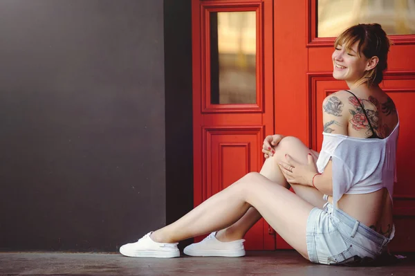 Retrato de una hermosa chica sentada en el suelo cerca de la puerta roja — Foto de Stock