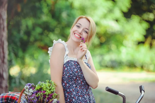 Hermosa mujer con una bicicleta en la naturaleza, feliz y saludable, flor tierna en las manos, estilo de vida saludable — Foto de Stock