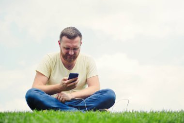 sakallı adam gökyüzü, yeşil teknolojileri ve ekoloji karşı yeşil çimenlerin üzerinde oturan bir telefon ücretleri